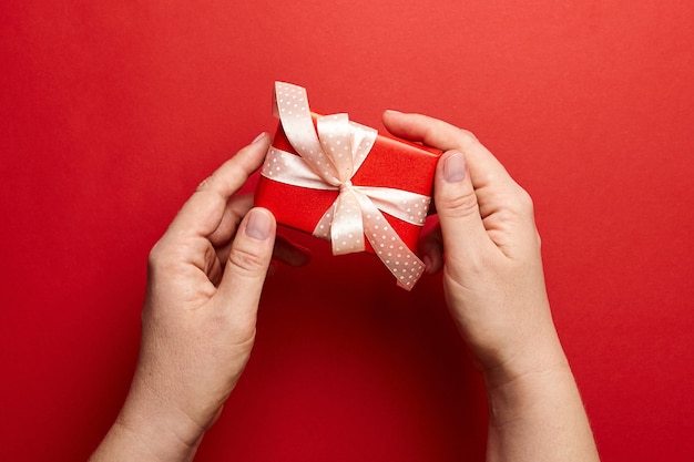 Hände, die Geschenkbox auf rotem Hintergrund halten