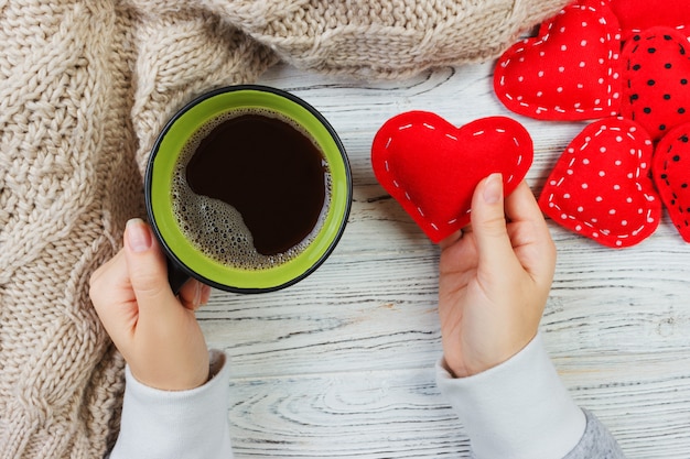 Hände, die Kaffeetasse und Textilherz halten