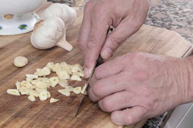 Hände, die Knoblauch auf dem Küchentisch beim Kochen brechen