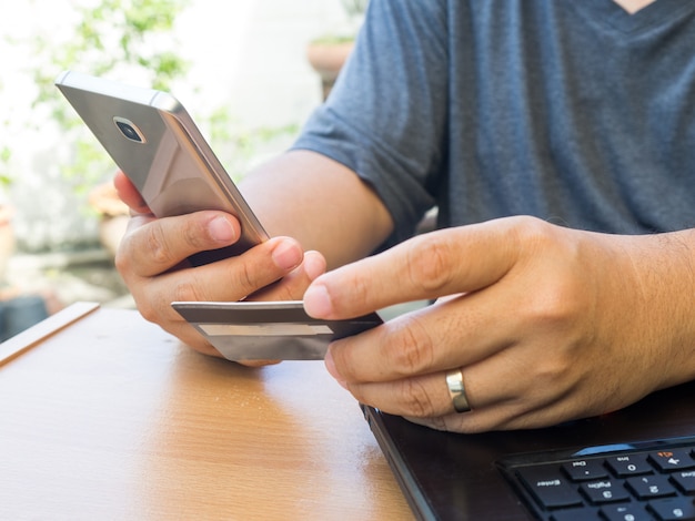 Hände, die Kreditkarte halten und intelligentes Mobiltelefon für das Online-Zahlungseinkaufen verwenden