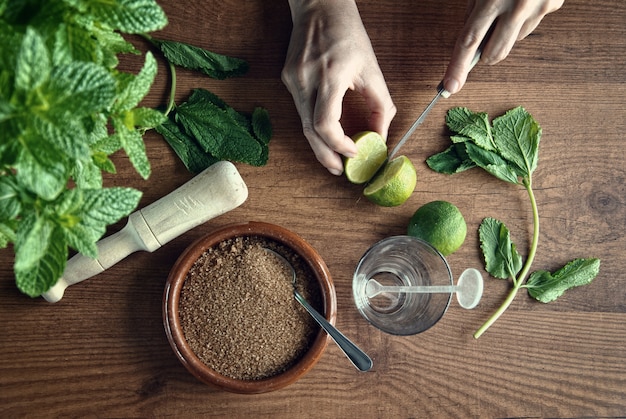 Hände, die Mojito-Cocktail mit Kalken und Minze vorbereiten