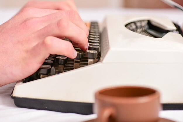 Foto hände, die retro-schreibmaschine eingeben alte schreibmaschine und autorenhände männliche hände geben geschichte oder bericht mit weißer vintage-schreibmaschinenausrüstung aus nächster nähe ein schreibroutine vintage-schreibmaschinenkonzept