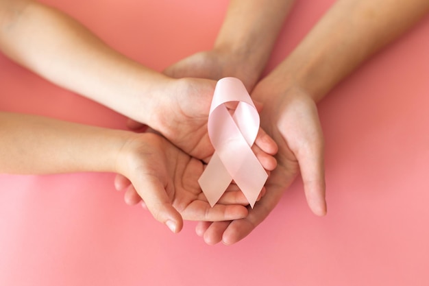 Hände, die rosa Schleife auf rosa Hintergrund halten Brustkrebs-Bewusstsein und Oktober-Rosa-Tag
