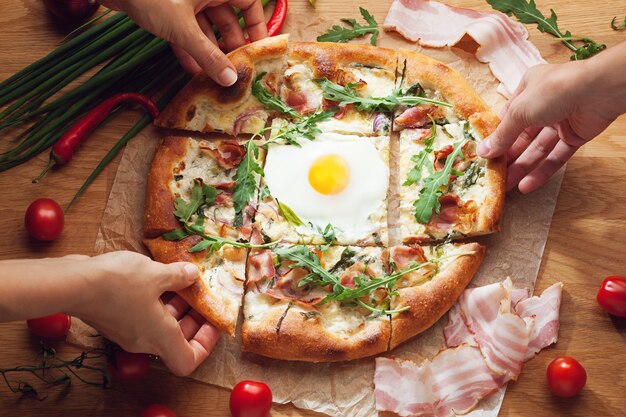 Hände, die Scheiben der köstlichen Pizza nehmen, die auf Holztisch serviert werden