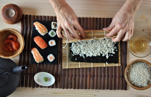 Hände, die Sushi mit Reis, Lachsen und Nori kochen