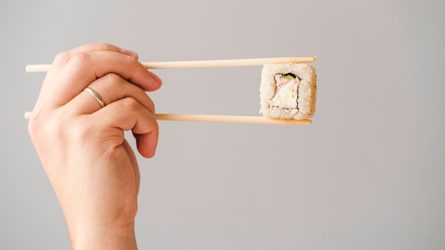 Hände, die Sushirolle mit Essstäbchen halten