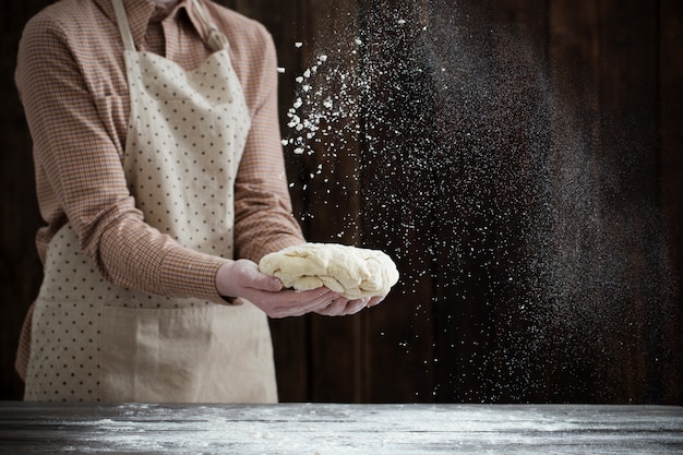 Hände, die Teig auf dunklem Holz kochen