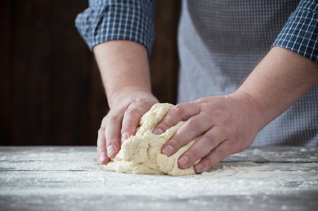 Hände, die Teig auf dunklem Holz kochen