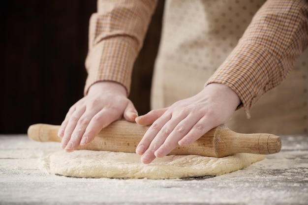 Hände, die Teig auf dunklem Holz kochen