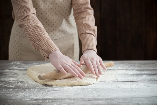 Hände, die Teig auf dunklem Holztisch kochen