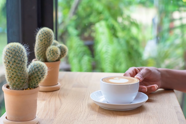 Hände, die weiße Kaffeetasse mit Untertasse auf Holztisch halten