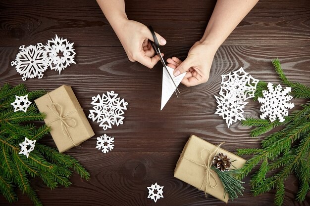 Hände, die weiße Papierschneeflocken auf Holztisch schneiden