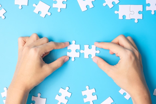 Hände, die weiße Puzzleteile des Paares auf blauem Hintergrund verbinden. Lösungskonzept, Mission, Erfolg, Ziele, Zusammenarbeit, Partnerschaft, Strategie und Puzzletag