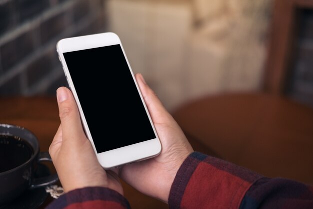 Hände, die weißes Mobiltelefon mit leerem schwarzem Schirm im Café halten und verwenden