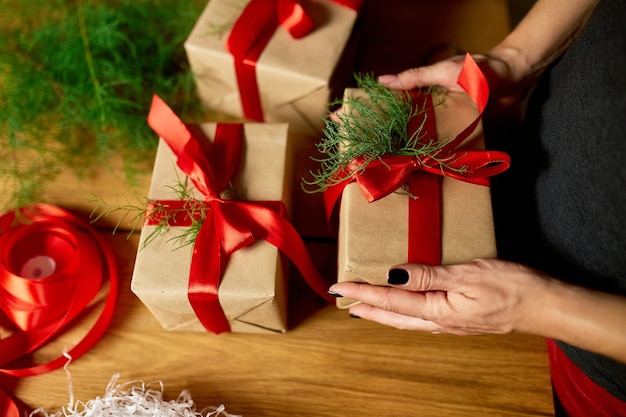 Hände einer abgeschnittenen, nicht erkennbaren Frau, die Weihnachtsgeschenk verpackt