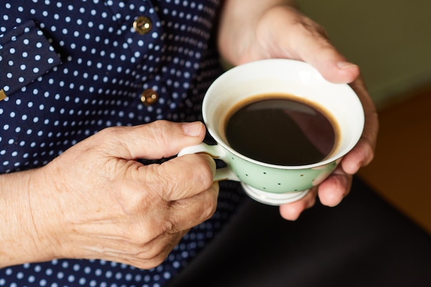 Hände einer älteren Frau, die eine Tasse Kaffee hält