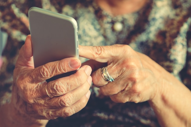 Hände einer älteren Frau, die einen Handy hält