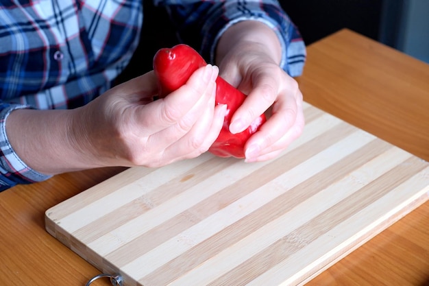 Hände einer älteren Frau, die in der Küche an einem braunen Tisch rote Paprikaschoten zeigt, kein Gesicht, Nahaufnahme