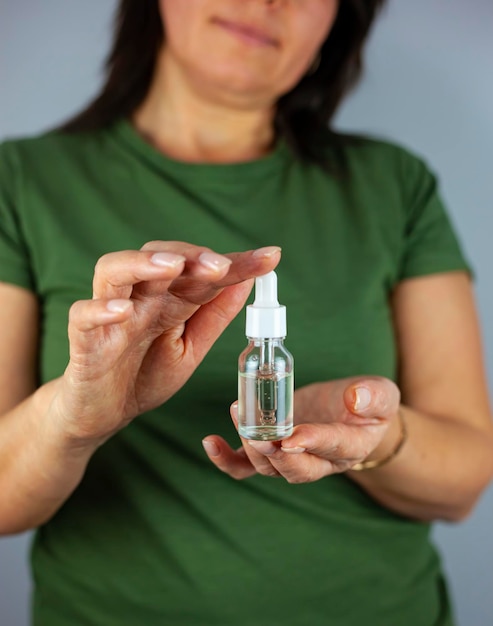 Hände einer beschnittenen weißen Frau, die eine Pipette mit kosmetischem Serum hält