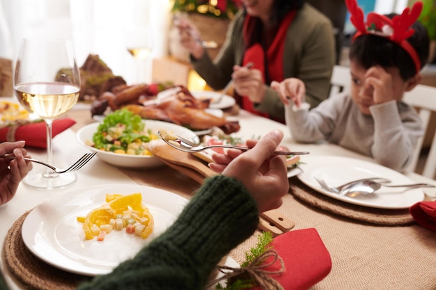 Hände einer Frau, die beim Weihnachtsessen mit ihrer Familie köstlichen Salat isst