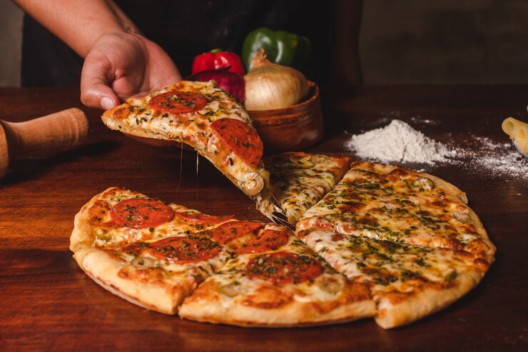 Foto hände einer frau, die ein stück pizza auf einem holztisch anhebt.