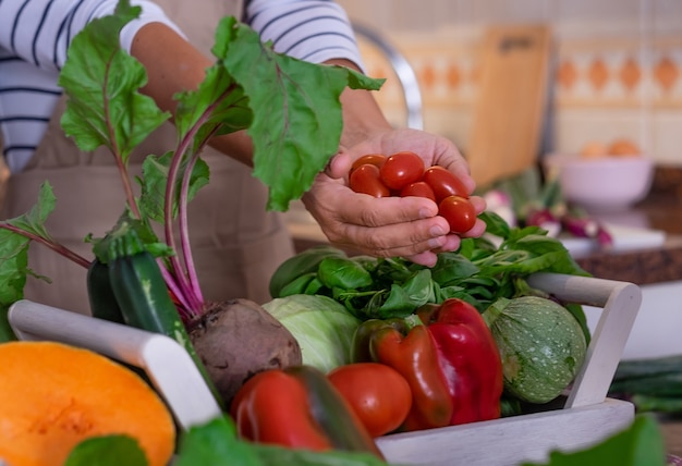 Hände einer Frau, die kleine rote Tomaten hält Mis von frischem Gemüse auf dem Tisch vegetarisches Konzept