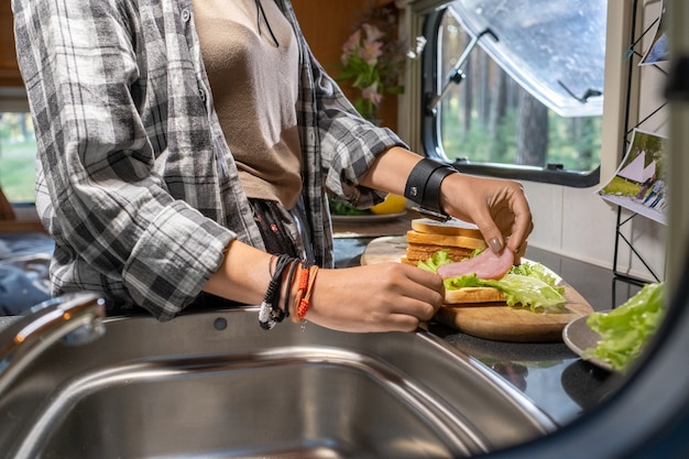 Hände einer Frau, die Speck und Salat auf ein Stück Brot legt