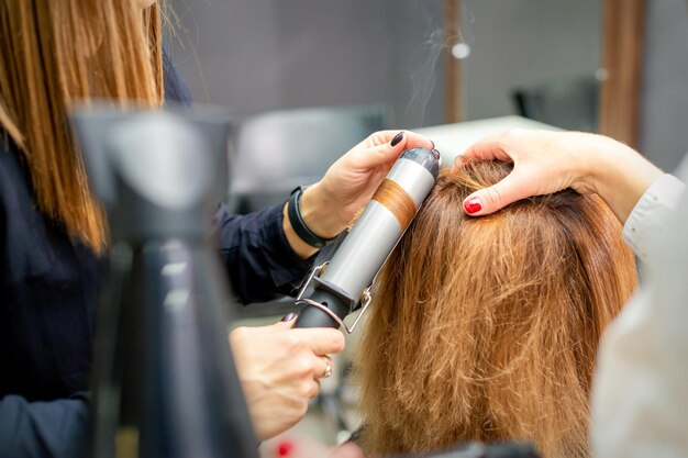Hände einer Friseurin lockt Haarkunden mit einem Lockenstab in einem Friseursalon, Nahaufnahme.