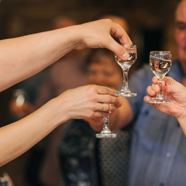Hände einer Gruppe Freunde, die Gläser Wodka klirren und den Feiertag feiern