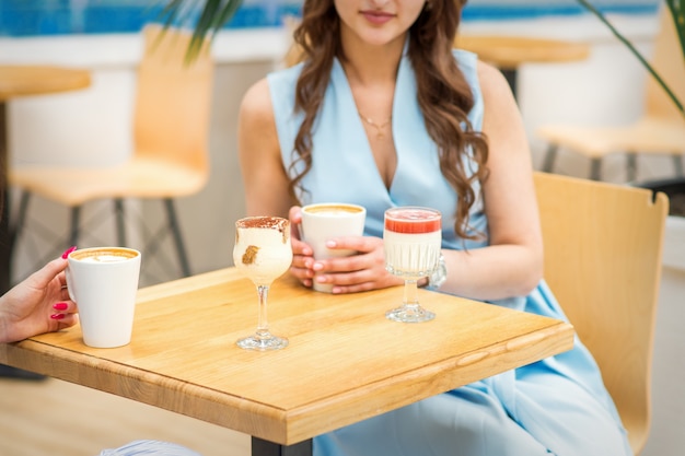 Hände einer jungen Frau, die eine Tasse Kaffee mit verschiedenen Cocktails auf dem Tisch im Café hält