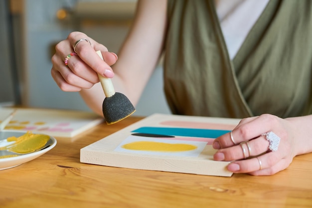 Hände einer jungen kreativen Frau mit Schwamm zum Auftragen von Gouache auf Papier