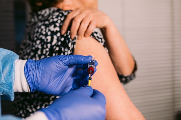 Hände einer Krankenschwester füllen die Spritze mit dem Impfstoff aus der Durchstechflasche, um einer älteren Frau einen Impfstoff in den Arm zu injizieren