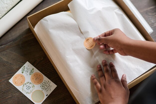 Hände einer Lagerarbeiterin, die Aufkleber auf Packpapier legt