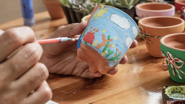 Hände einer lateinischen Mulattin, die Tontöpfe malt, um Sukkulenten zu pflanzen