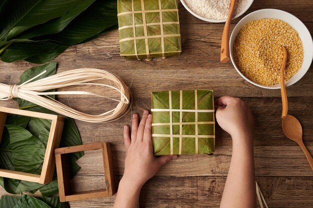 Hände einer Person, die traditionellen vietnamesischen Klebreiskuchen in Lotusblätter einwickelt