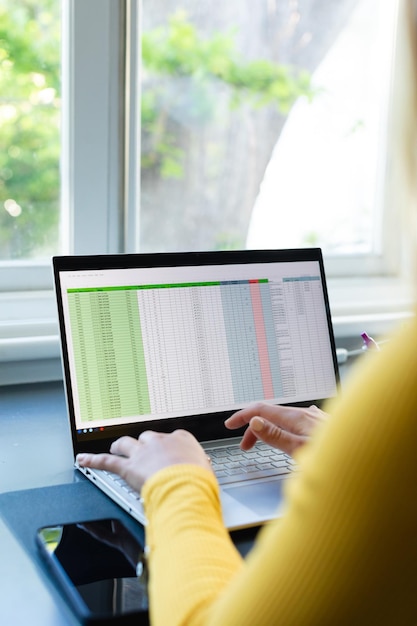 Foto hände einer weißen frau, die an einem schreibtisch sitzt, von zu hause aus arbeitet und einen laptop in einem sonnigen raum benutzt