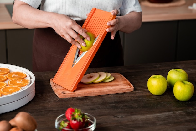 Hände einer zeitgenössischen Hausfrau, die Scheiben frischer Äpfel auf eines der Tabletts mit Obsttrockner legt, während sie für den Winter sorgen