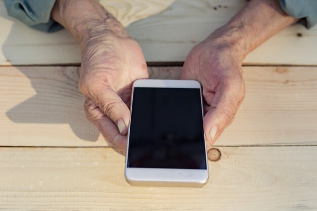 Hände eines älteren Mannes, der ein Telefon hält und benutzt. Das Konzept, älteren Menschen neue Technologien beizubringen, Kommunikation mit der älteren Generation. Bild.