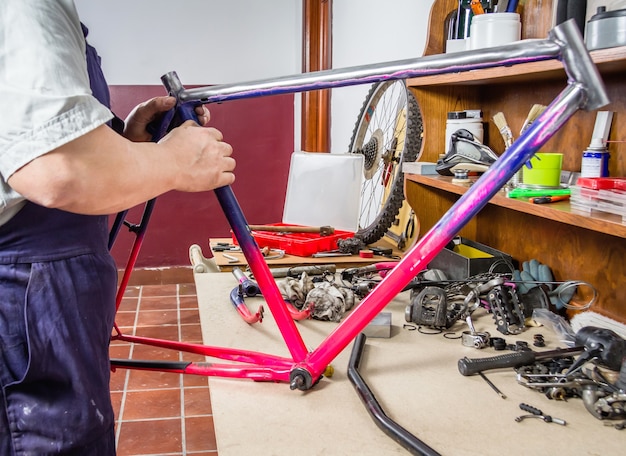 Hände eines echten Fahrradmechanikers, der beschädigtes Rahmenfahrrad in einer Werkstatt säubert