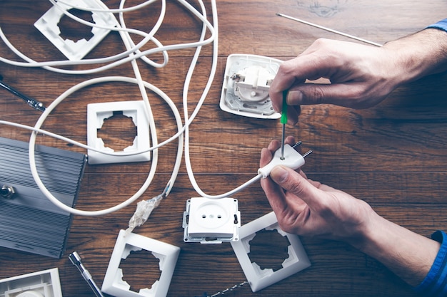 Hände eines Elektrikers, der einen Schraubendreher hält und am Stecker eines Elektrikers arbeitet