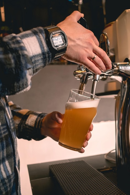 Hände eines erfahrenen Barkeepers, der ungefiltertes Craft-Bier aus dem Zapfhahn ins Glas gießt