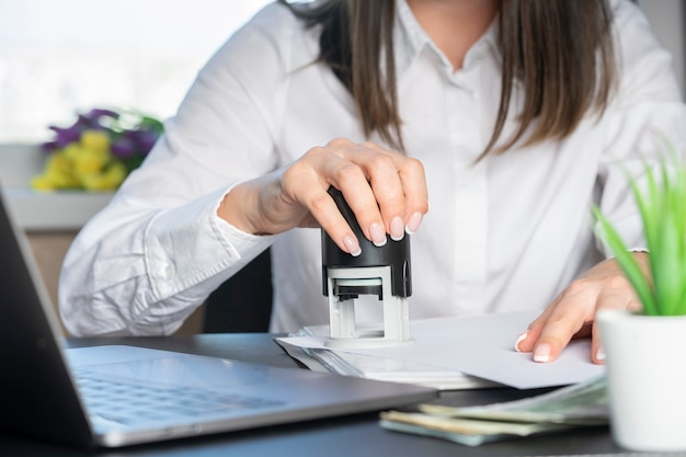 Hände eines Finanzarbeiters in einem weißen Hemd, das einen Stempel auf eine Dokumentnahaufnahme setzt.