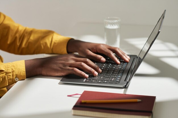 Hände eines jungen afroamerikanischen männlichen Analysten oder Maklers, der Laptoptasten drückt