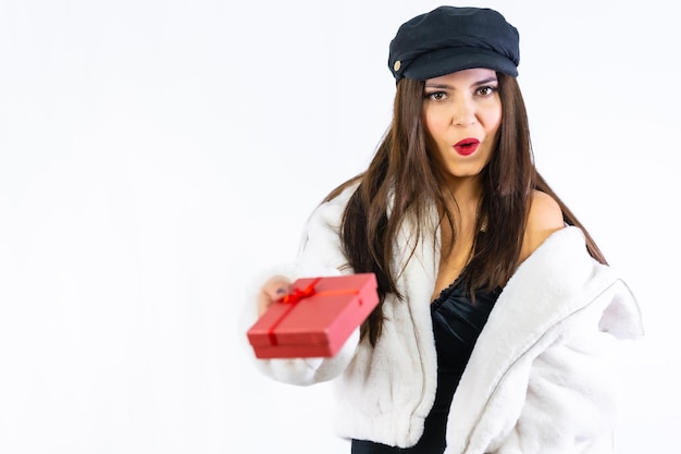 Hände eines jungen lateinischen Brunettemädchens, das freudig ein Geschenk auf einem weißen Hintergrund überreicht. Portrait des Models mit einer sehr aufgeregten roten Geschenkbox