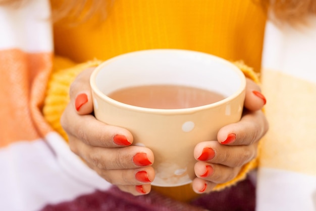 Hände eines jungen Mädchens, das Tasse mit heißem Tee hält