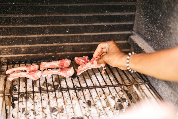 Hände eines lateinischen Mannes, der Schweinerippchen auf den Grill legt