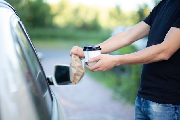 Hände eines Mannes, der Tassen Kaffee und eine Tasche anbietet