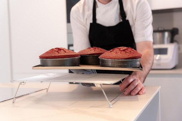 Hände eines Mannes, der zu Hause einen roten Samtkuchen kocht Biskuitkuchen, der in den Ofenformen gebacken wird