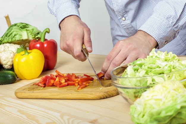 Hände eines Mannes gehackte rote Paprika für Salat auf einem Brett, Nahaufnahme