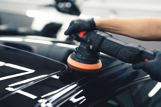 Hände eines Mannes mit Orbitalpolierer in der Werkstatt, der schwarze Sportwagen, Nahaufnahme, Auto poliert